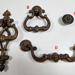 May include: Four antique brass cabinet hardware pulls. The first pull is a decorative ornate design with a pointed bottom. The second pull is a simple ring design. The third pull is a round knob with a floral design. The fourth pull is a curved handle with a decorative design.