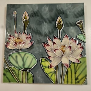 May include: Square ceramic tile featuring a detailed floral design. The artwork depicts white lotus flowers with red-tipped petals, green leaves, and stems against a mottled gray background. The tile is likely for decorative use.