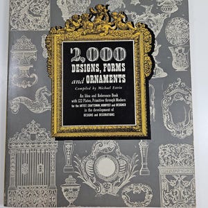 May include: A book cover with a gray background and gold trim. The title is "2,000 Designs, Forms and Ornaments" and the subtitle is "An Idea and Reference Book with 122 Plates, Primitive through Modern for the Artist, Craftsman, Hobbyist and Designer in the development of Designs and Decorations". The cover is decorated with various black and white illustrations of designs and ornaments.