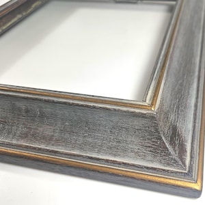 May include: A rectangular picture frame featuring a distressed finish with dark gray and black wood grain textures. The frame edges are accented with a thin, metallic gold trim along the inner and outer borders, creating a layered appearance.