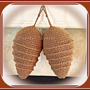 May include: Two brown crocheted pinecones hanging from a white surface. The pinecones are made with a spiral pattern and have a textured surface.