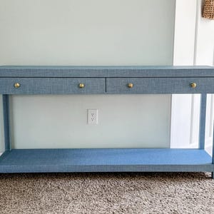 May include: A blue console table with two drawers and a lower shelf. The table has gold-colored knobs and a textured surface. The table is approximately 60 inches long, 16 inches deep, and 30 inches high.