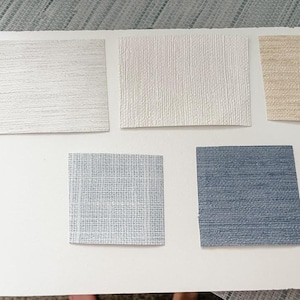 May include: Five samples of wallpaper in different colors and textures. The samples are arranged in two rows, with three samples in the top row and two samples in the bottom row. The samples are all rectangular and have a textured surface. The colors of the samples are white, beige, light blue, and dark blue.
