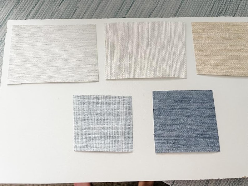 May include: Five samples of wallpaper in different colors and textures. The samples are arranged in two rows, with three samples in the top row and two samples in the bottom row. The samples are all rectangular and have a textured surface. The colors of the samples are white, beige, light blue, and dark blue.