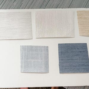 May include: Five samples of wallpaper in different colors and textures. The samples are arranged in two rows, with three samples in the top row and two samples in the bottom row. The samples are all rectangular and have a smooth, textured surface. The colors of the samples are white, beige, light blue, and dark blue.