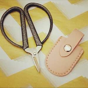 May include: Gold-toned nail clippers with a pink leather case. The clippers have a textured finish and a silver blade.