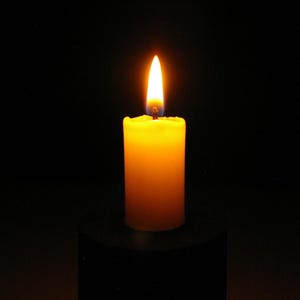 Puede incluir: Una vela amarilla encendida con una llama naranja brillante sobre un fondo negro. La vela es cilíndrica y parece estar hecha de cera. La llama es alta y delgada, emitiendo un brillo cálido.