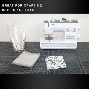 May include: A white sewing machine with a black cutting mat, a white fabric with black and white print, a white fabric square, and a gold wire basket with clear plastic tubes.