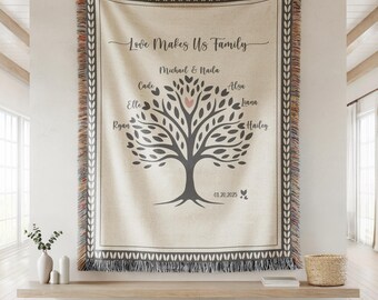 May include: A cream-colored woven throw blanket featuring a dark gray tree illustration with the text Love Makes Us Family, names Michael, Naila, Cade, Alsa, Elle, Liana, Ryan, Hailey, and the date 01.20.2025, finished with a multicolored fringe border.