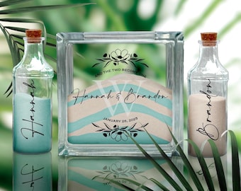 May include: A clear glass sand ceremony set with a large glass block and two bottles. The block contains layers of sand in blue and beige, with the names "Hannah & Brandon" and the date "January 26, 2025". The bottles are labeled with the names "Hannah" and "Brandon".