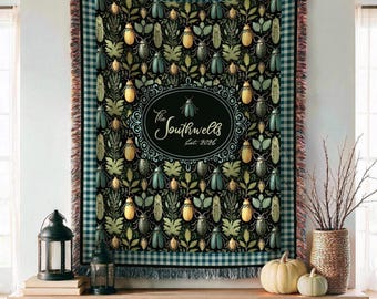 May include: A woven throw blanket featuring a repeating pattern of beetles and foliage on a black background, bordered by a blue and white gingham check. The center displays an oval frame with the text The Southwells Est. 2026 and a beetle.