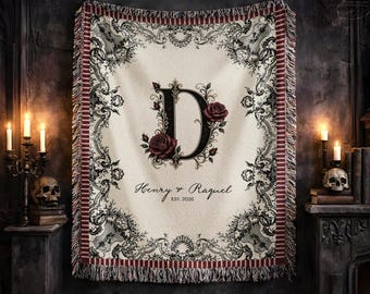 May include: A cream-colored woven throw blanket featuring a large black letter D surrounded by dark red roses. The blanket has a decorative black filigree border and fringed edges. Text on the blanket reads Henry & Raquel and EST. 2026.