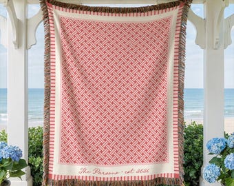May include: A woven throw blanket featuring a coral and cream geometric basketweave pattern with a striped border. The bottom edge displays the text The Parsons est 2021 in a script font. The blanket has a multi-colored fringed edge on all sides.