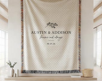 May include: A woven throw blanket with a cream and beige textured pattern, featuring black text that reads AUSTIN & ADDISON, forever and always, and the date 08.07.26, topped with a small leaf sprig graphic and finished with multicolored fringe.