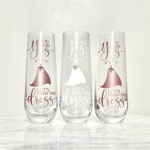 Pu&ograve; includere: Tre flute da champagne con la scritta "You said yes, let's find the dress" su di esse. Le flute sono in vetro trasparente con un design color oro rosa.