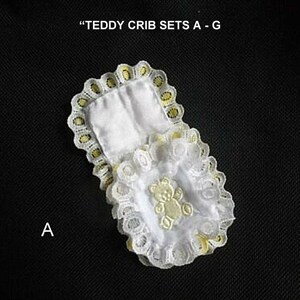 May include: White lace crib set with yellow trim and a small embroidered teddy bear. "Teddy Crib Sets A-G" is written above the crib set. The letter "A" is written below the crib set.