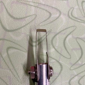 May include: A silver metal tool with a handle and a small blade at the top. The handle has a textured grip.