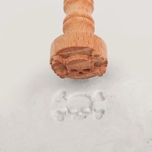 May include: A wooden stamp with a skull and crossbones design. The stamp is being used to create an impression in a white substance.