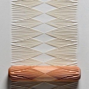 May include: A wooden rolling pin with a carved design of overlapping triangles. The rolling pin is used to create a decorative pattern on clay or dough.