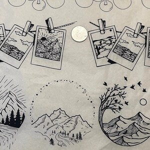 May include: A collection of black and white line drawings of mountains, trees, and sunrises. The drawings are arranged in a grid pattern on a brown paper background. Some of the drawings are framed in a Polaroid-style frame.