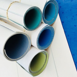 May include: Five rolls of white fabric with different coloured edges. The edges are blue, green and yellow.