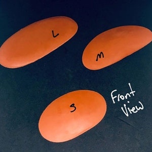 May include: Three orange oval-shaped cushions labelled with the letters "L", "M", and "S" on a dark background. The text "Front View" is written below the cushions.