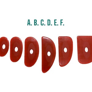 May include: A set of six red pottery rib tools in different shapes and sizes, each with a central hole. The tools are displayed in a row against a white background, with the letters A to F above.
