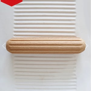 May include: A wooden drawer pull with a grooved design. The pull is light brown and has rounded ends.