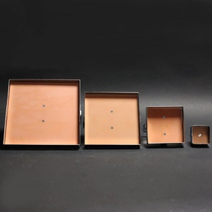 May include: Four square metal frames with a light brown interior. The frames are arranged in descending size order from left to right.