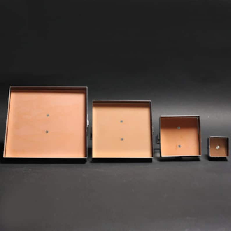 May include: Four square metal frames with a light brown interior. The frames are arranged in descending size order from left to right.