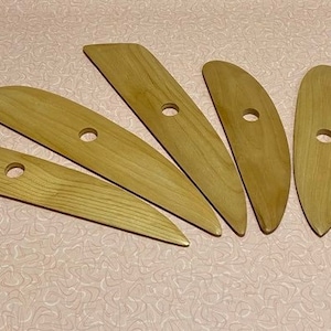 May include: Six wooden sculpting tools with holes in the handles. The tools are different shapes and sizes, and are arranged in a fan shape.