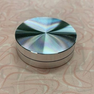 May include: A silver metal knob with a circular, slightly domed top. The knob has a smooth, shiny surface and a subtle, concentric pattern.