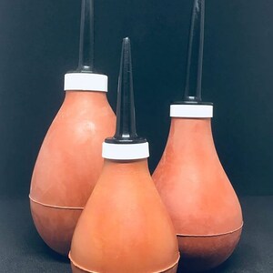 May include: Three red rubber bulb syringes with black tips and white bands. The syringes are arranged in a row, with the largest syringe at the back and the smallest syringe at the front.