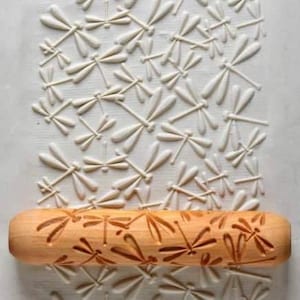 May include: A wooden rolling pin with a dragonfly design. The rolling pin is used to create decorative patterns in dough.