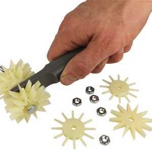May include: A tool for creating decorative patterns in clay or dough. It features a grey handle with a rotating wheel with multiple spokes. The wheel is made of white plastic and can be replaced with other wheels. The image also shows several spare wheels and nuts.