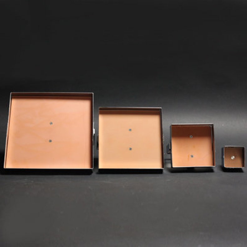 May include: Four square metal frames with a light brown interior. The frames are arranged in descending size order from left to right.