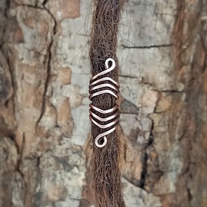 Op de afbeelding: Een dreadlock-kraal van koperdraad met een spiraalvormig ontwerp. De kraal is om een dreadlock gewikkeld.