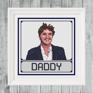 Może przedstawiać: Portret krzyżykowy uśmiechniętej osoby w granatowej marynarce i białej koszuli. Słowo "DADDY" jest wyświetlane w szarym banerze pod portretem, oprawionym w biały kwadrat z granatową obwódką. Grafika jest w białej ramie.