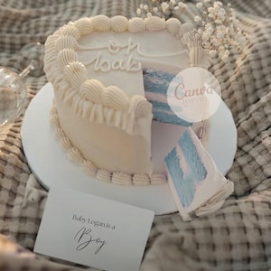 May include: A two-layer cake with white frosting and blue filling, decorated with piped frosting and small white flowers. The cake has a slice removed, revealing the blue interior. A card reads "Baby Logan is a Boy."