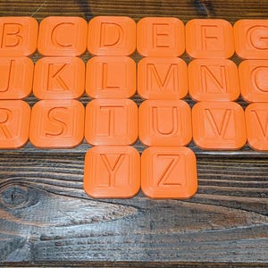 May include: Orange alphabet letter tiles with rounded edges. Each tile features a single uppercase letter in a white font.