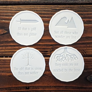 May include: Four white ceramic coasters with embossed images and quotes from The Lord of the Rings. The quotes are: "All that is gold does not glitter", "Not all those who wander are lost", "The old that is strong does not wither", and "Deep roots are not reached by the frost."