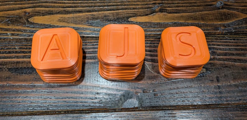 May include: Three orange plastic blocks stacked on top of each other, spelling out the word "AJS".