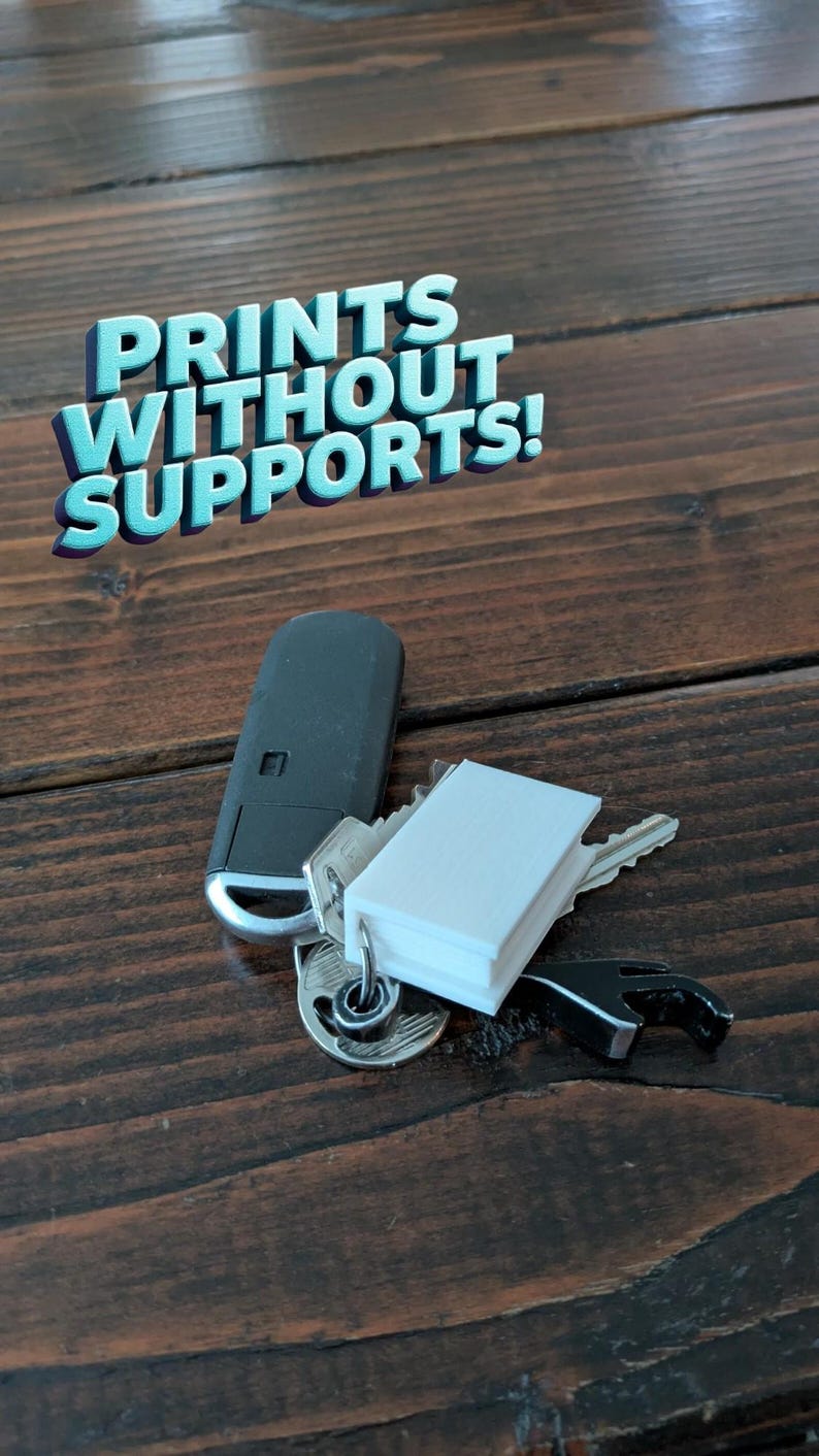 May include: A set of keys, a car key fob, and a small white object on a key ring rest on a dark brown wooden surface. The text "PRINTS WITHOUT SUPPORTS!" is displayed in a 3D font.
