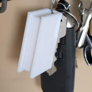 May include: A set of white, rectangular key tags hanging on a key ring with a car key and other keys. The key tags are made of a solid, opaque material and have a smooth surface. The key tags are attached to a metal hook.