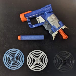 Könnte beinhalten: Eine blaue und orange Spielzeugpistole mit einem blauen Pfeil und drei kreisförmigen Zielen, einem blauen, einem weißen und einem schwarzen.