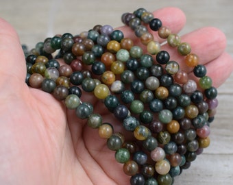 May include: A strand of round, multi-colored agate beads. The beads are a mix of green, brown, and yellow with some red and purple accents. The beads are approximately 6mm in diameter.