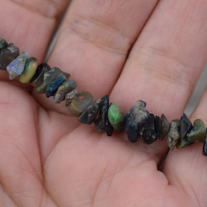 May include: A strand of black and green opal chip beads. The beads are irregular in shape and size, and have a natural, rough finish.