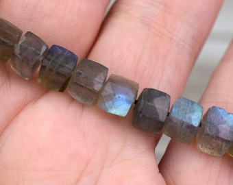 May include: A strand of faceted labradorite beads in shades of grey, blue, and green. The beads are square-shaped and have a smooth, polished finish.