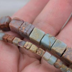 May include: A strand of brown, green and blue gemstone beads. The beads are square shaped and have a mottled pattern.