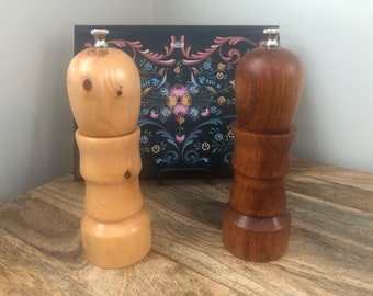May include: Two wooden salt and pepper shakers with silver tops. The shaker on the left is light wood and the shaker on the right is dark wood.